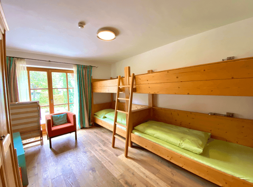 Helles Kinderzimmer mit Etagenbetten, Holzboden und Blick ins Grüne durch das große Fenster.