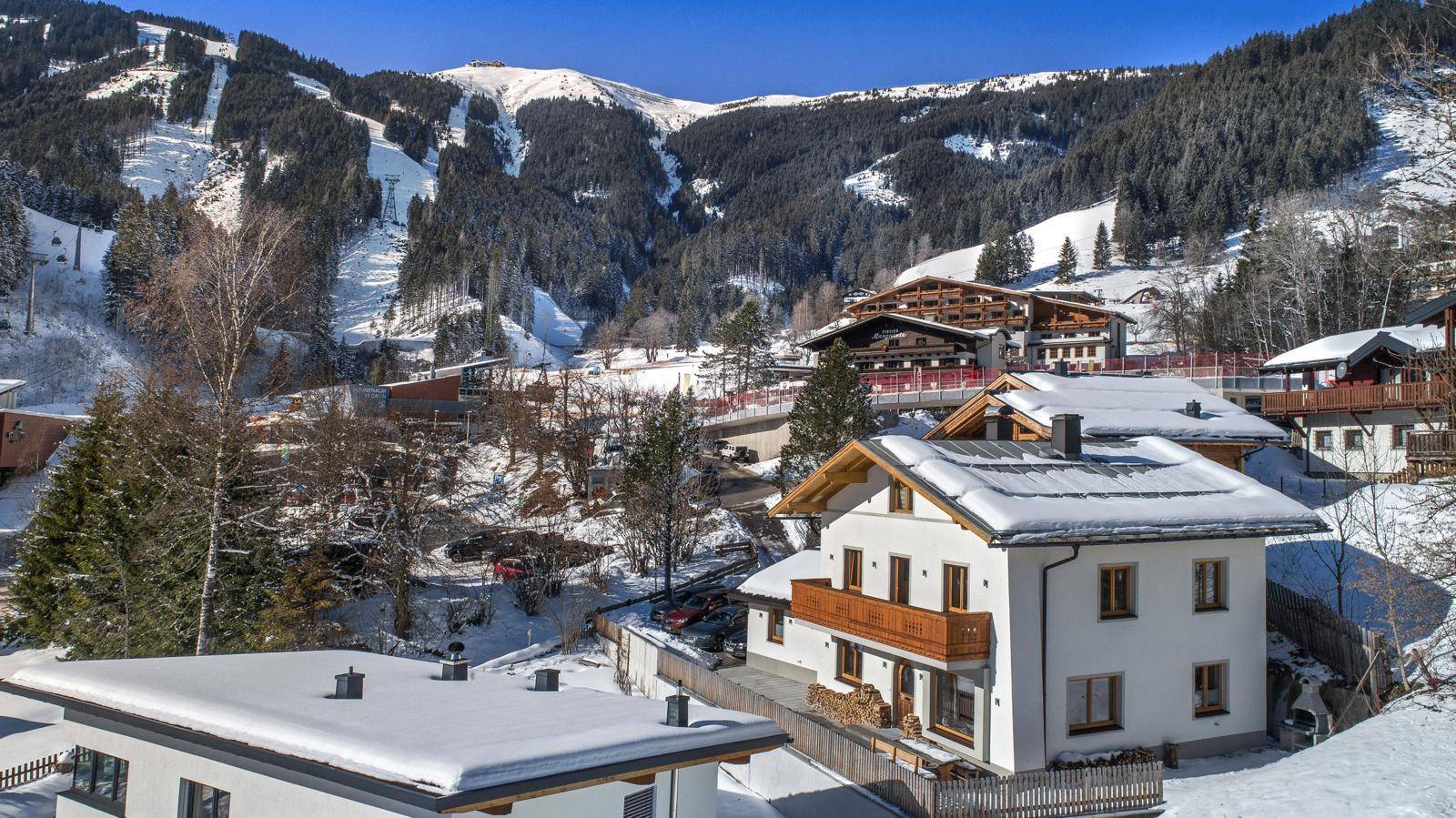 Charmantes Haus in verschneiter Berglandschaft mit Holzbalkon und Blick auf die Skipisten.
