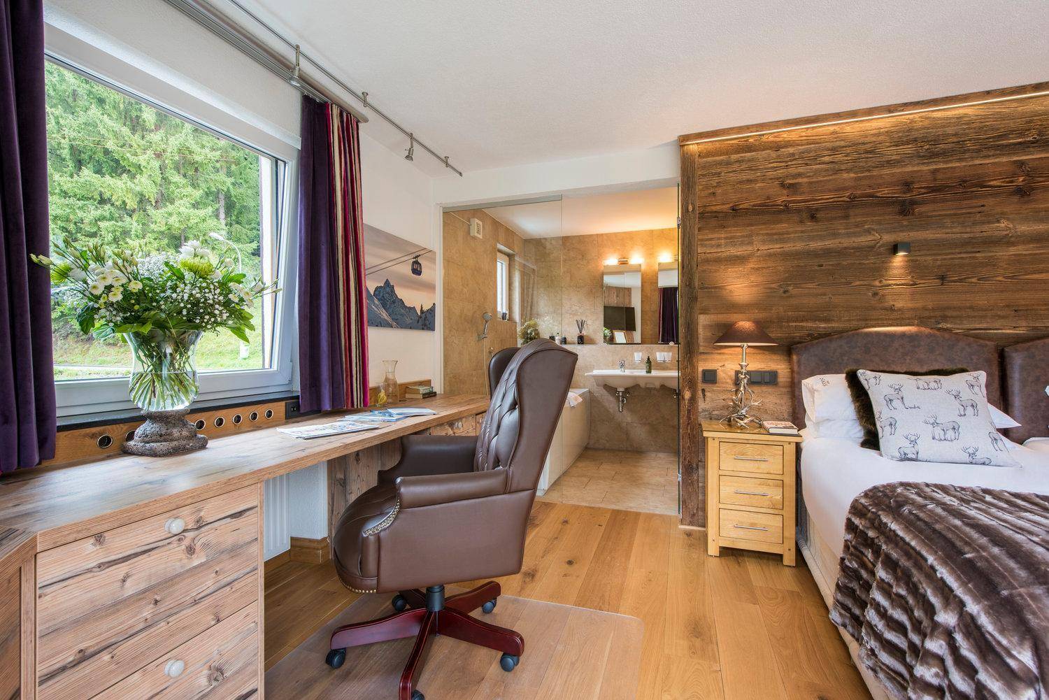 Komfortables Schlafzimmer mit Holzwand, Schreibtisch und offenem Zugang zum Badezimmer.