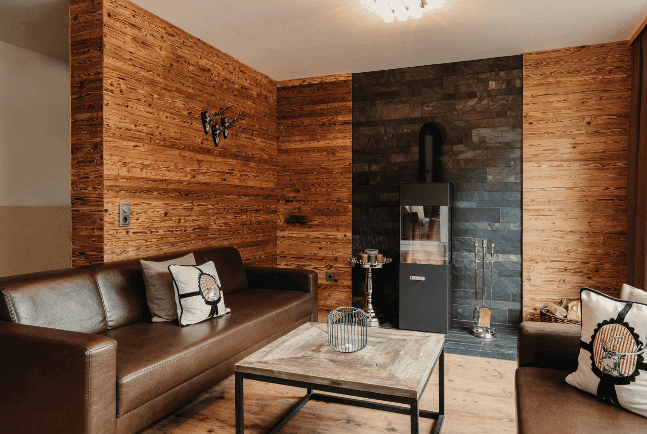 Rustikales Wohnzimmer mit Holzwänden, Kaminofen und traditioneller Hirschgeweih-Dekoration.