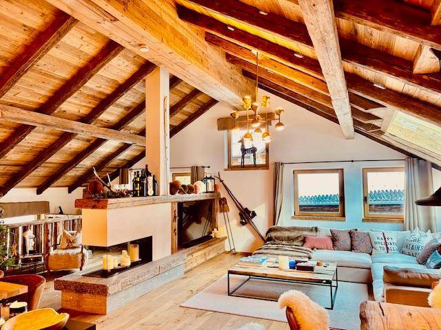 Gemütliches Wohnzimmer im alpinen Stil mit freiliegenden Holzbalken, Kamin und Blick auf die Berge.