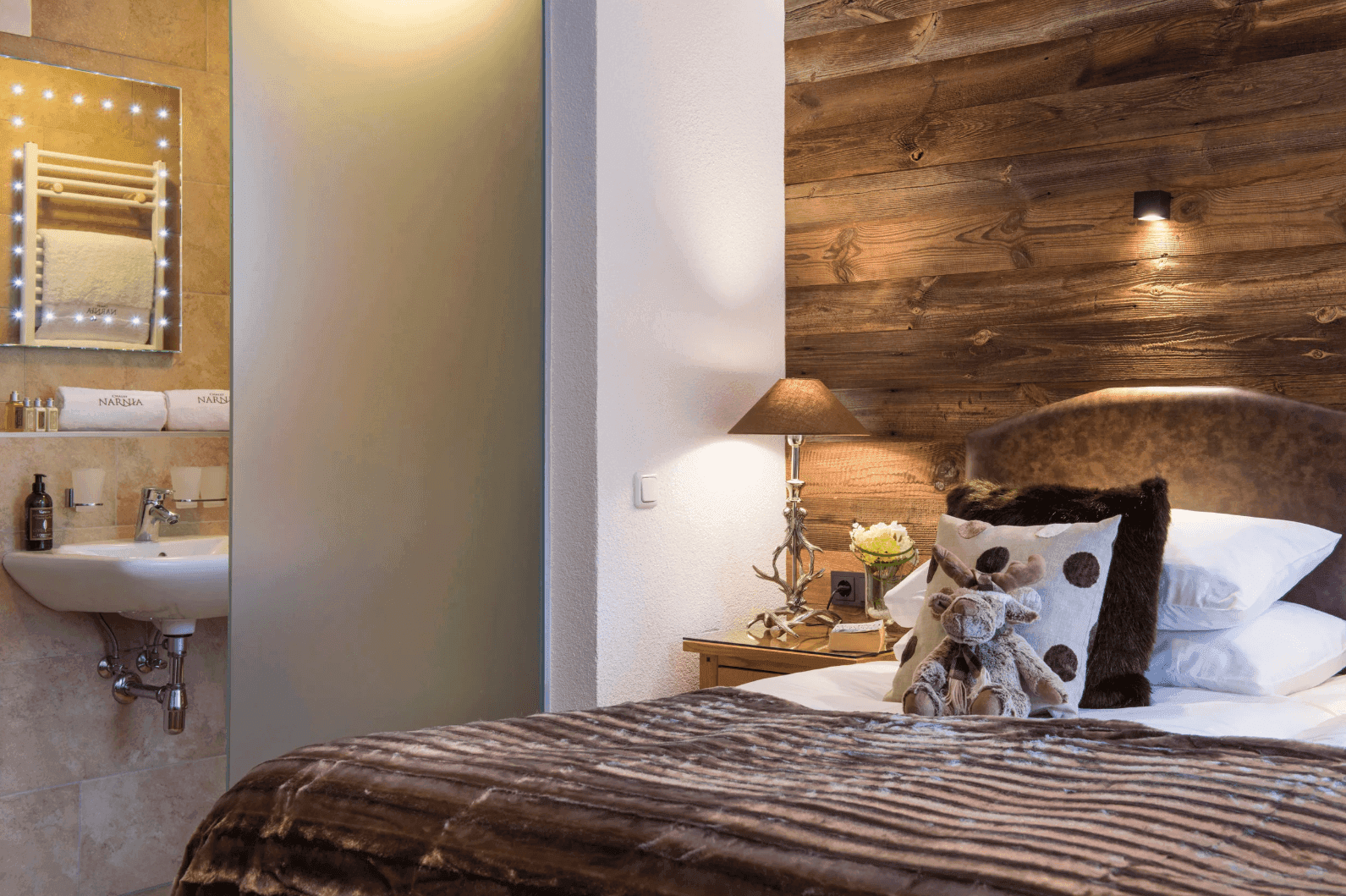 Schlafzimmer mit Holzwand und angrenzendem Badezimmer, ausgestattet mit modernem Waschbecken.