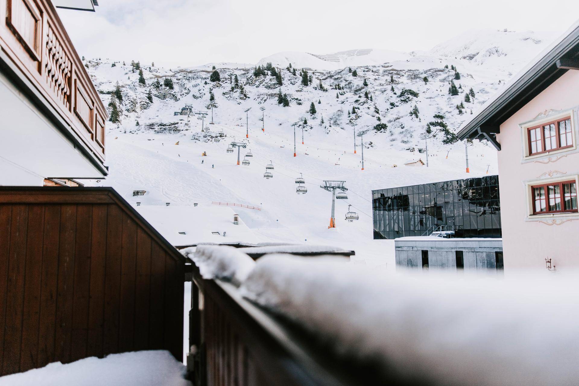 Blick von einem Balkon auf die verschneite Berglandschaft mit Skiliften und modernen Gebäuden.
