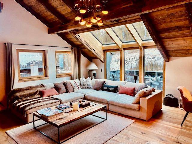 Helles Wohnzimmer mit großem Ecksofa, Holzbalkendecke und großen Fenstern mit Bergblick.