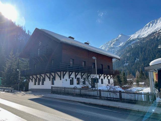 Alpines Holzhaus mit schneebedecktem Dach und Balkonen an einem sonnigen Wintertag.