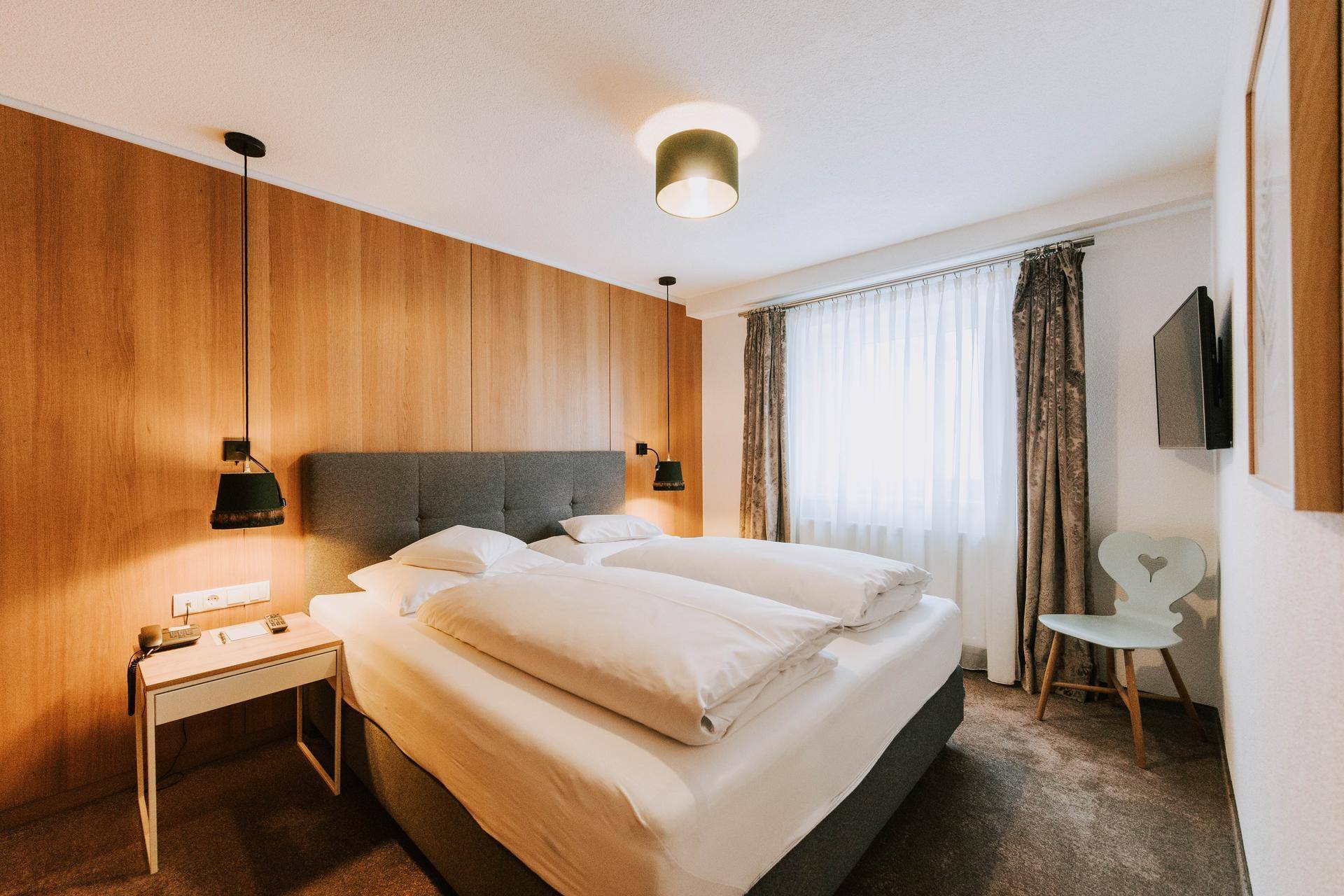 Komfortables Schlafzimmer mit Holzwand, Doppelbett, Teppichboden und Blick nach draußen.