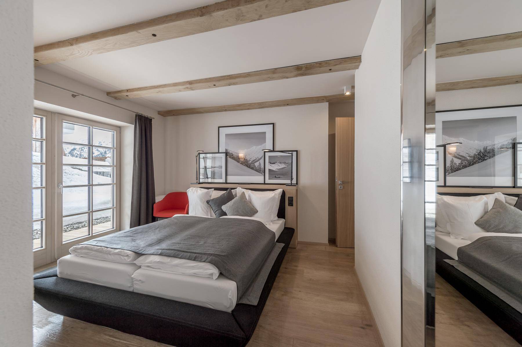 Modernes Schlafzimmer mit Holzbalken, Doppelbett und Spiegelwand, hell und einladend.