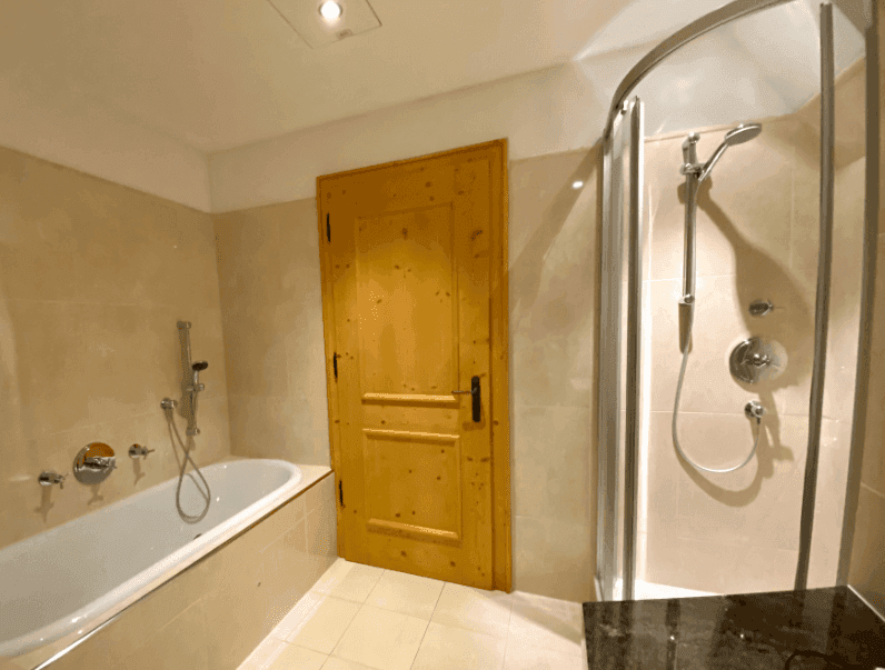 Modernes Badezimmer mit Badewanne, Duschkabine und Holztür in hellen Farbtönen.