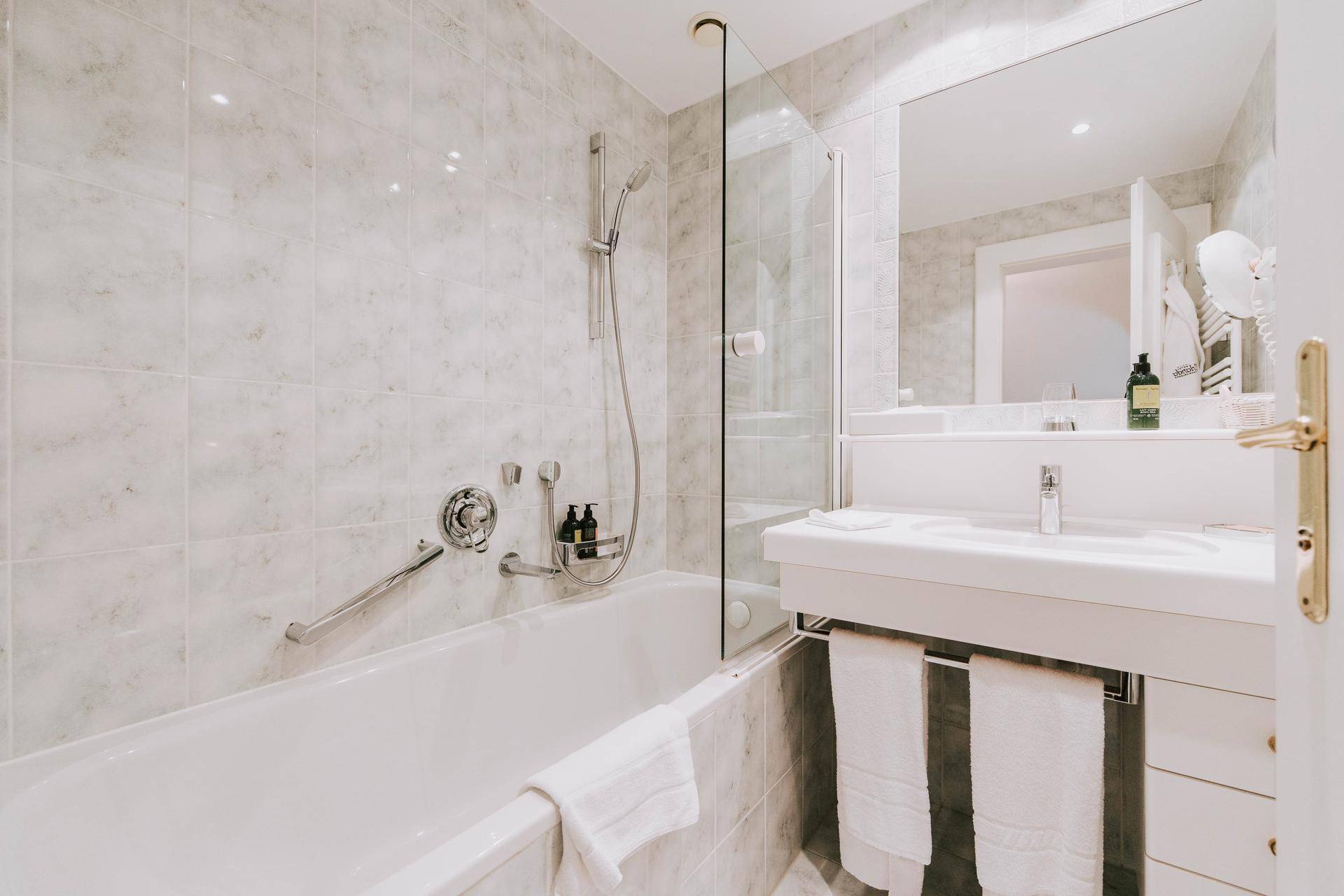Helles Badezimmer mit Badewanne, Duschabtrennung, Waschtisch und Marmorfliesen.