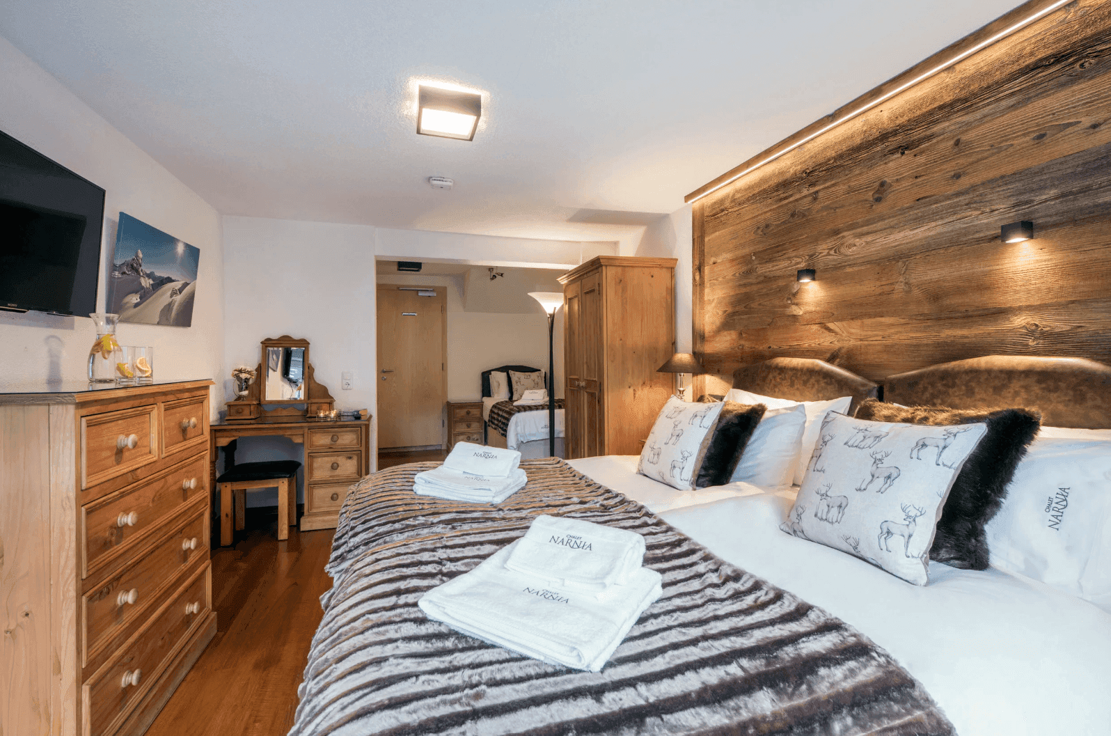 Geräumiges Schlafzimmer mit Doppelbett, Holzboden, Schminktisch und Blick in den Nebenraum.