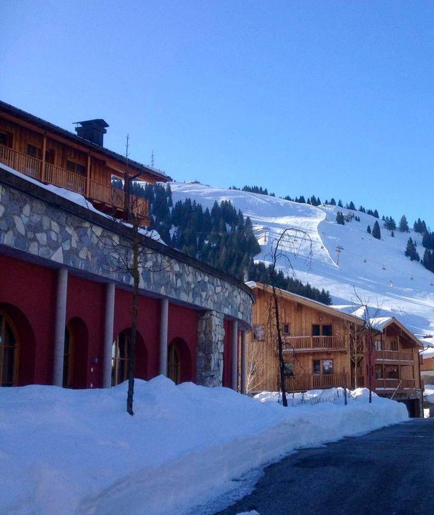 Gebäude mit Steinfassade und Holzelementen in einer tief verschneiten Winterlandschaft mit Skipiste.