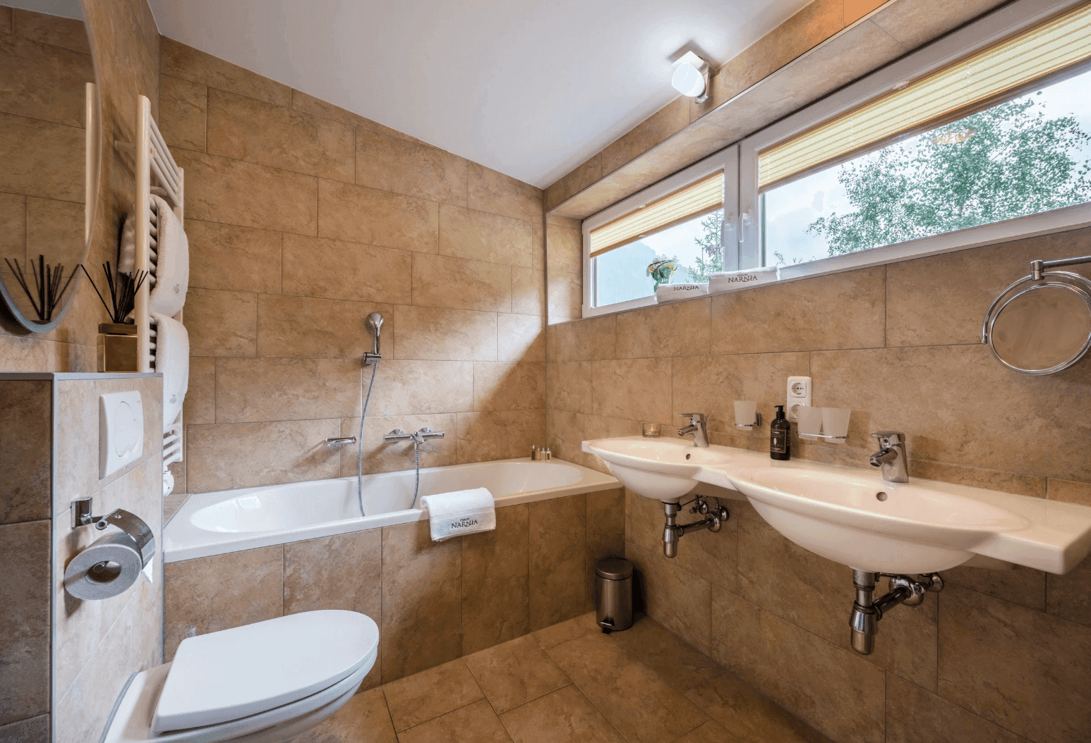 Geräumiges Badezimmer mit Badewanne, Doppelwaschbecken und Fenster mit Blick ins Grüne.