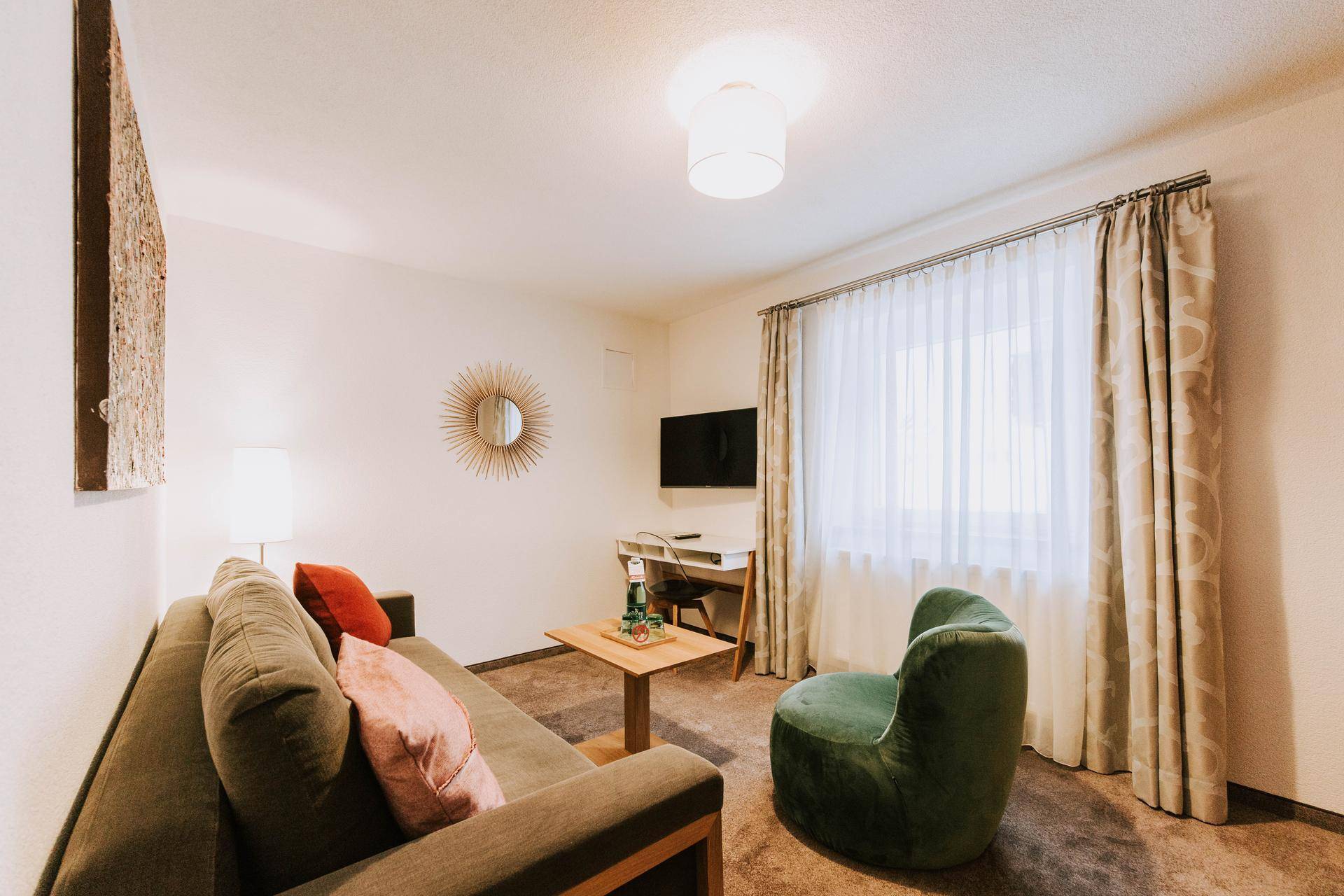 Helles Wohnzimmer mit Sofa, Sessel, Couchtisch und Teppichboden in neutralen Farben.