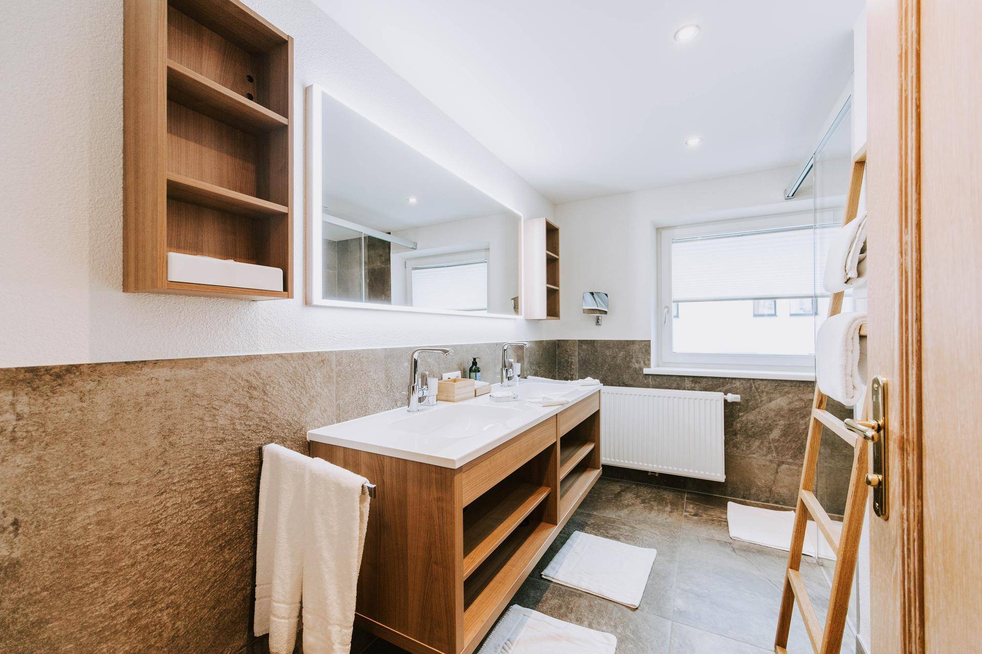 Modernes Badezimmer mit Doppelwaschtisch, großem beleuchteten Spiegel und Fliesenboden.