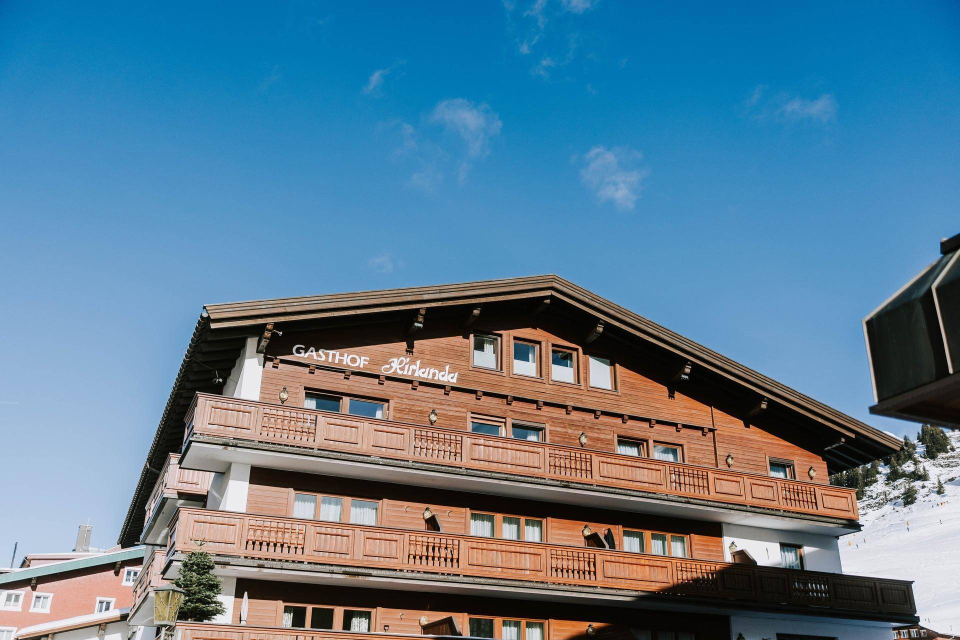 Das Hotel Kirlana mit traditioneller Holzfassade und Balkonen unter strahlend blauem Himmel.