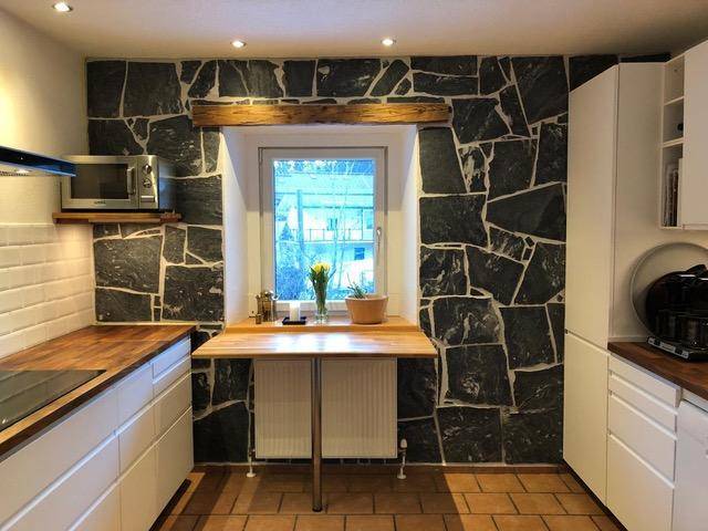 Moderne Küche mit weißen Schränken, Holztheke und einer Steinwand als Akzent.