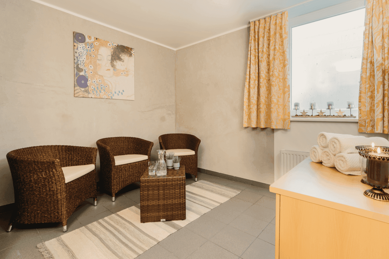 Entspannungsbereich mit Korbsesseln, kleinem Tisch und Fenster mit gelben Vorhängen.