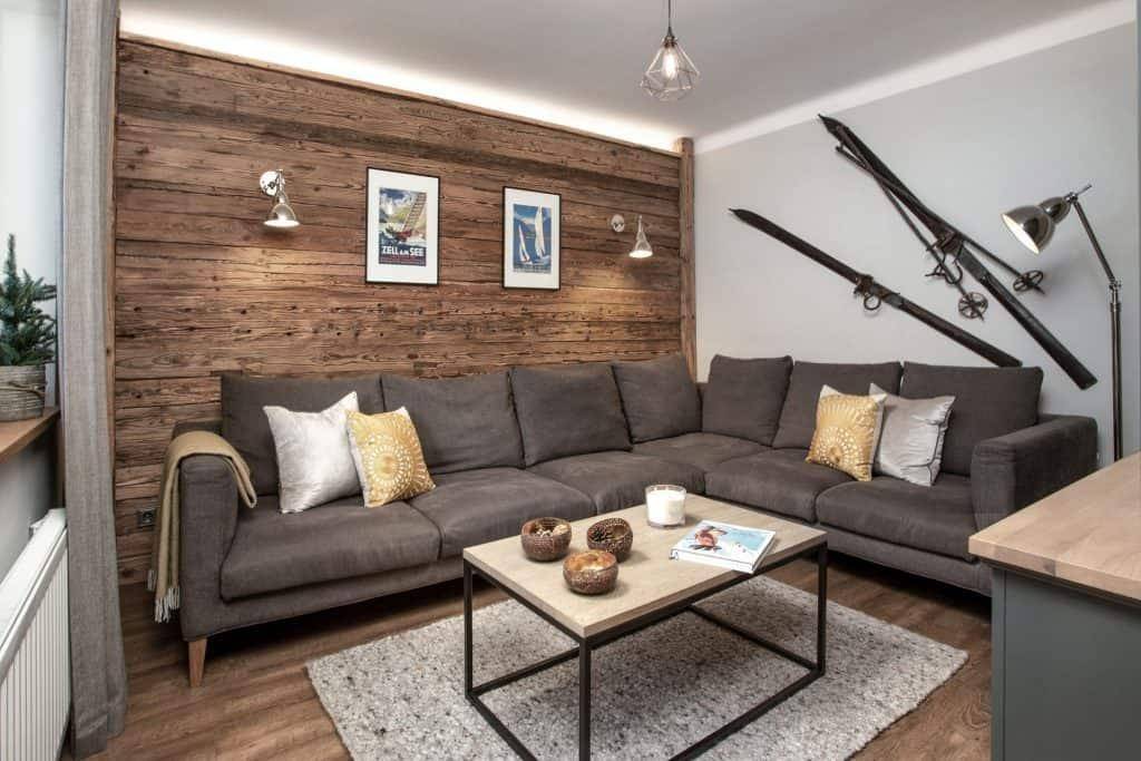 Gemütliches Wohnzimmer mit Holzwand, großem Ecksofa und rustikalen Skiern als Dekoration.