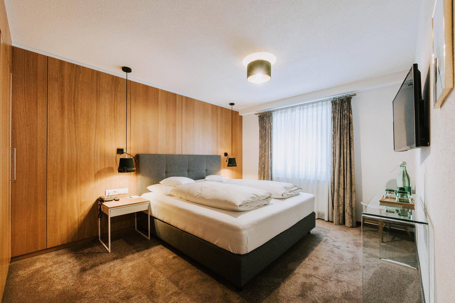 Gemütliches Schlafzimmer mit Holzwand, Doppelbett und Teppichboden in warmen Farbtönen.