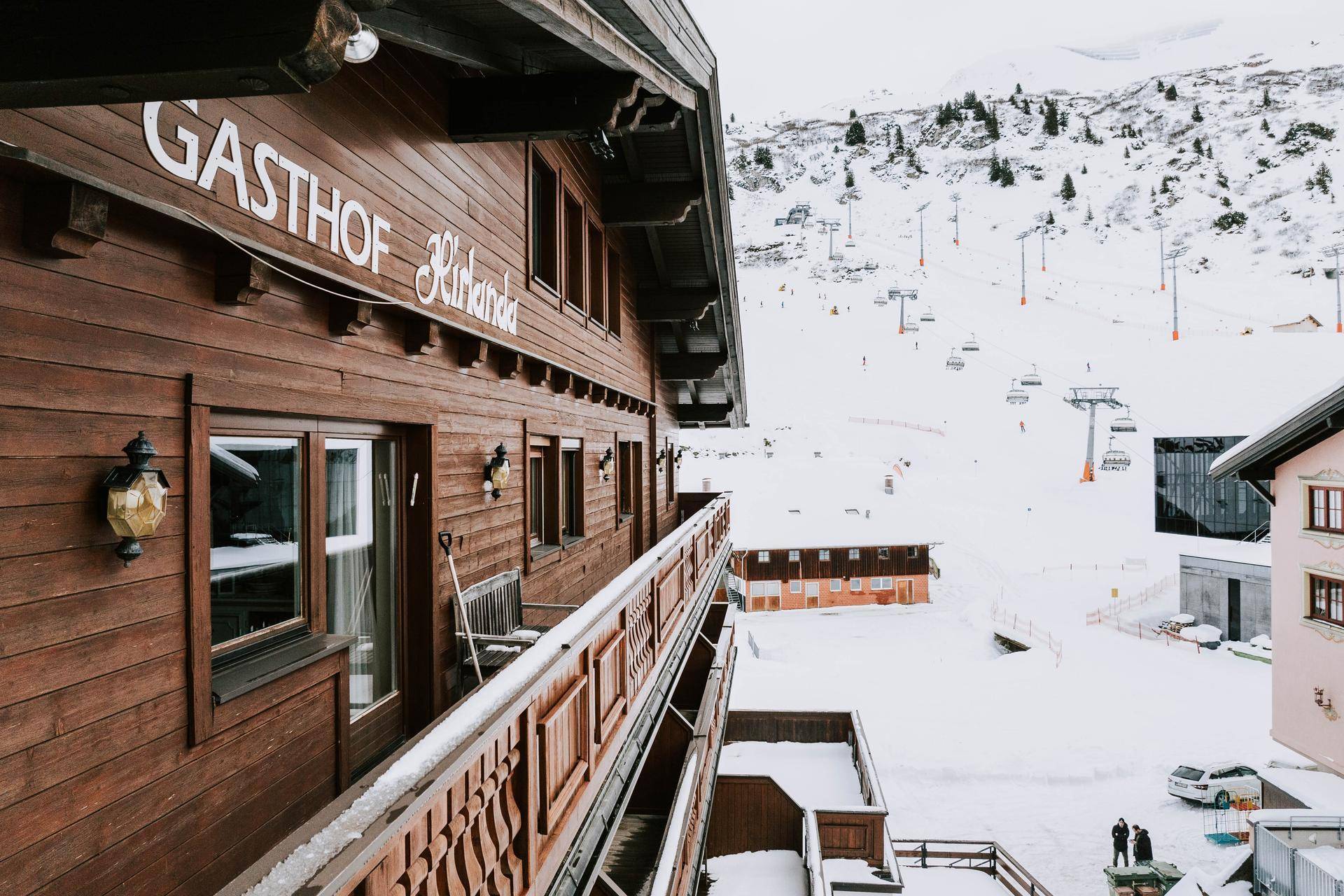 Traditioneller Holzbalkon des Gasthofs Kirlana mit Blick auf die verschneite Berglandschaft und Skilifte.