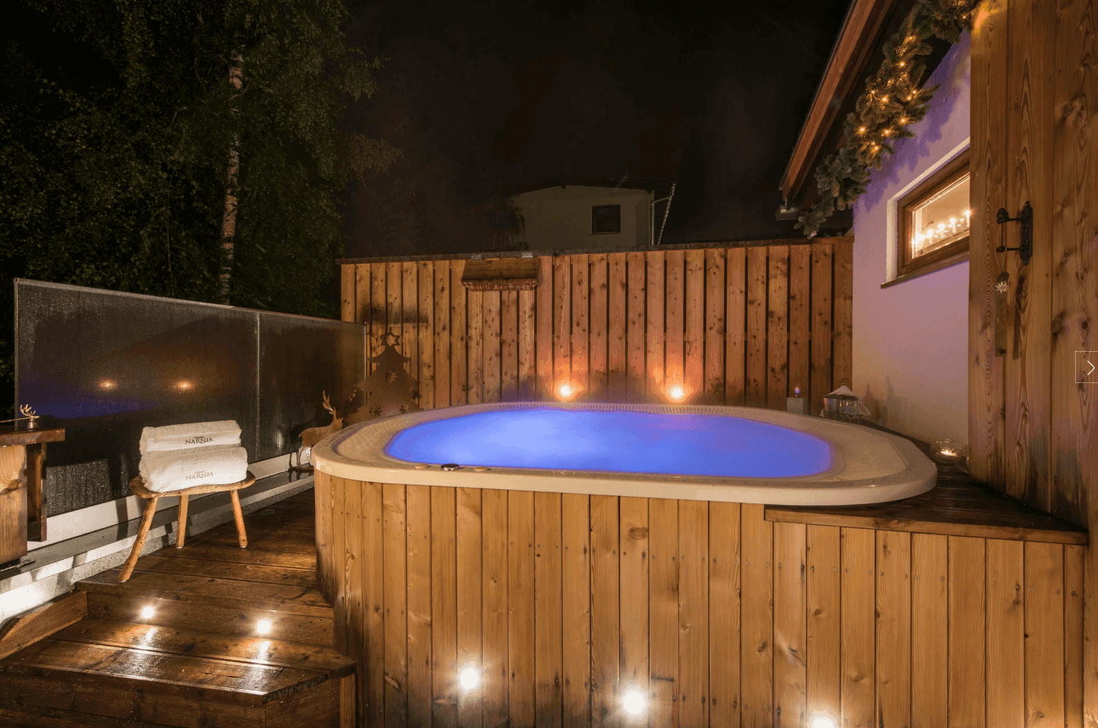 Beleuchteter Whirlpool im Freien mit Holzverkleidung und stimmungsvoller Beleuchtung bei Nacht.