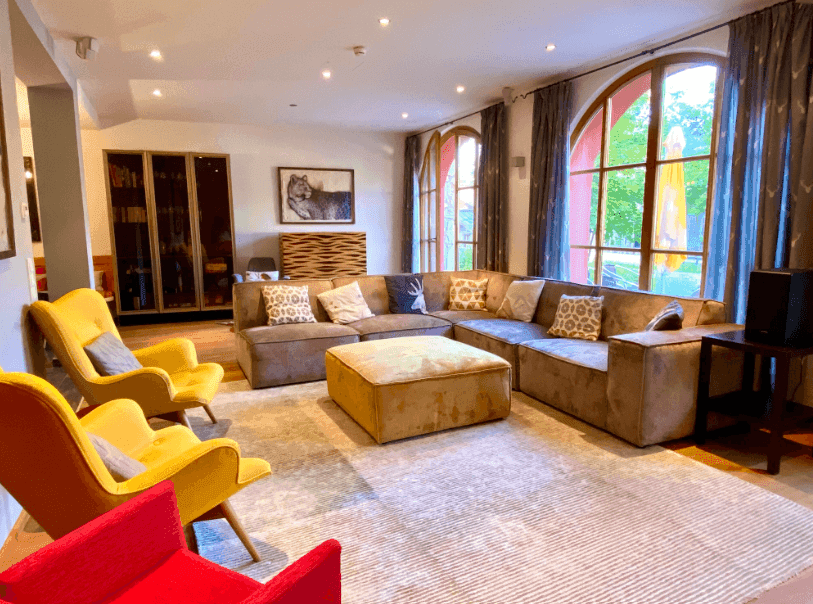 Geräumiges Wohnzimmer mit großem Ecksofa, farbigen Sesseln und großen Rundbogenfenstern.