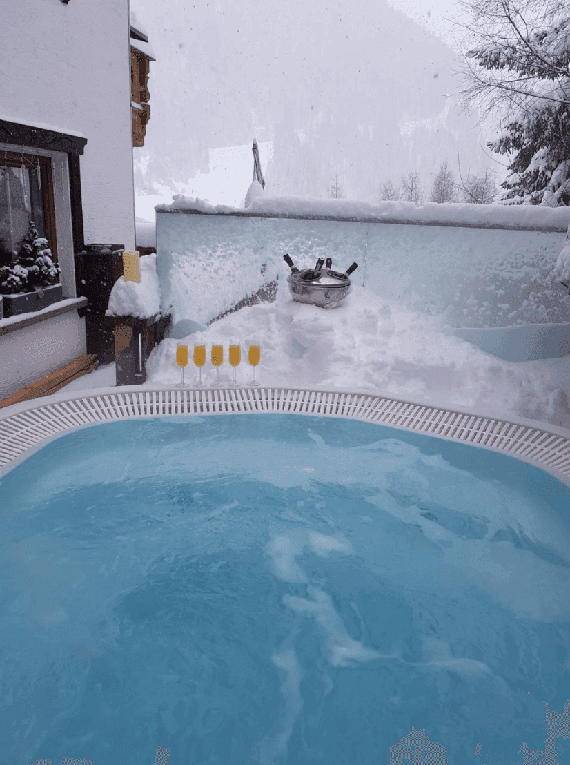Whirlpool im Freien umgeben von Schnee und Eis, mit Gläsern bereit für ein Getränk.