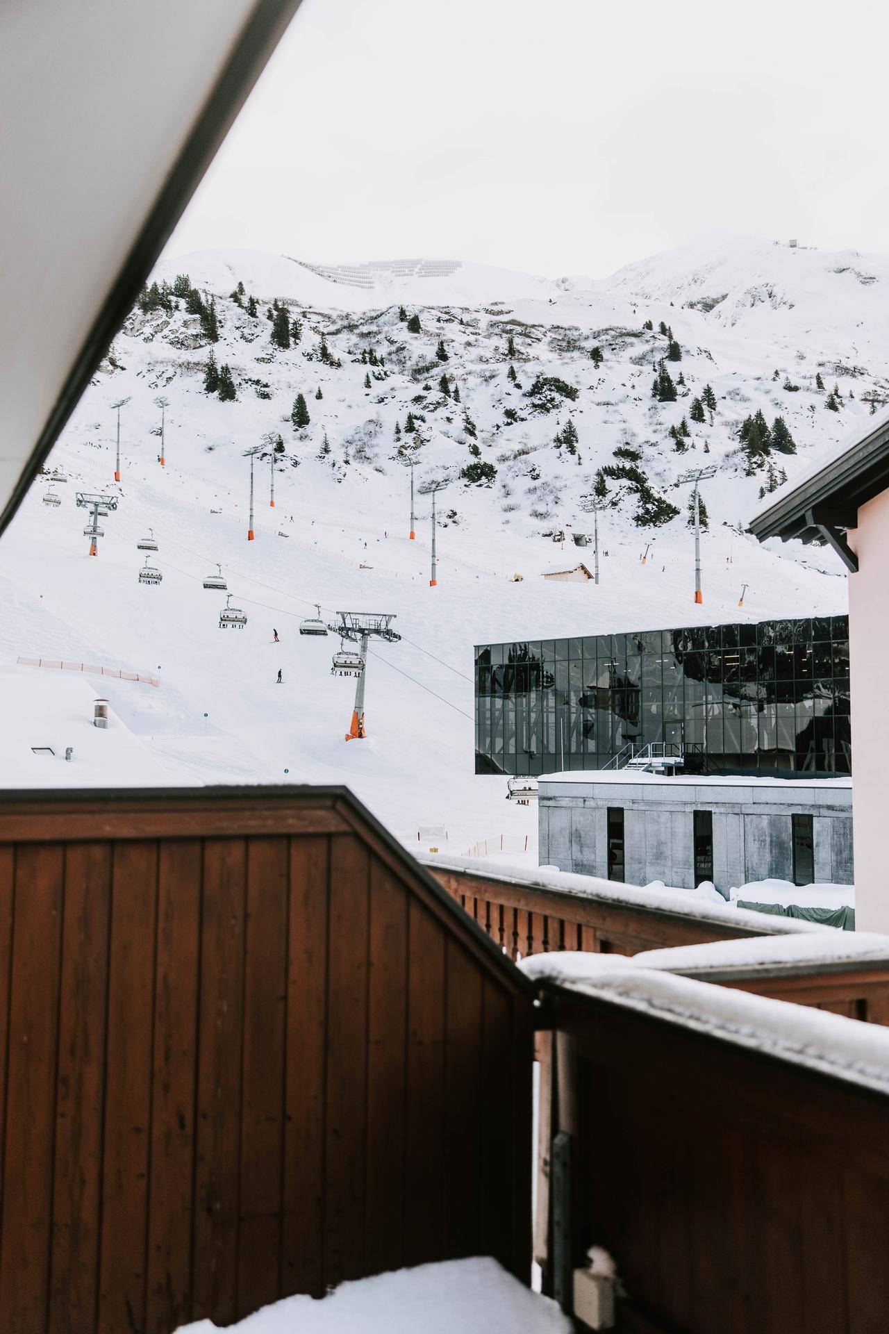 Blick von einem Balkon auf die verschneite Berglandschaft mit Skiliften und modernen Gebäuden.