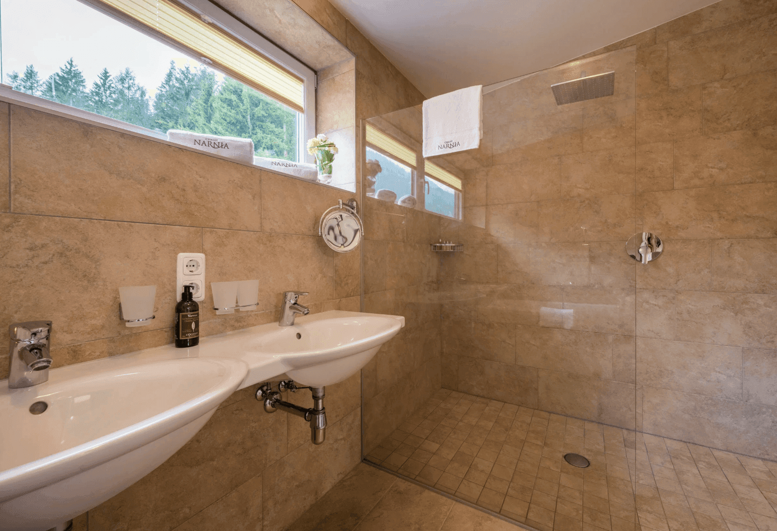 Modernes Badezimmer mit ebenerdiger Dusche, Doppelwaschbecken und Fenster mit Waldblick.