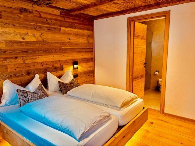 Schlafzimmer im alpinen Stil mit Holzwänden und direktem Zugang zu einem modernen Badezimmer.