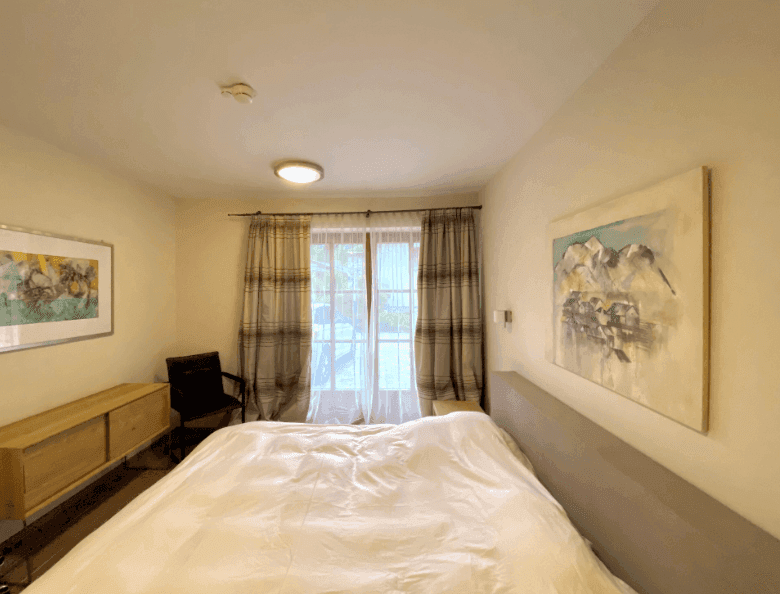 Helles Schlafzimmer mit Holzboden und großem Fenster, das viel Tageslicht hereinlässt.