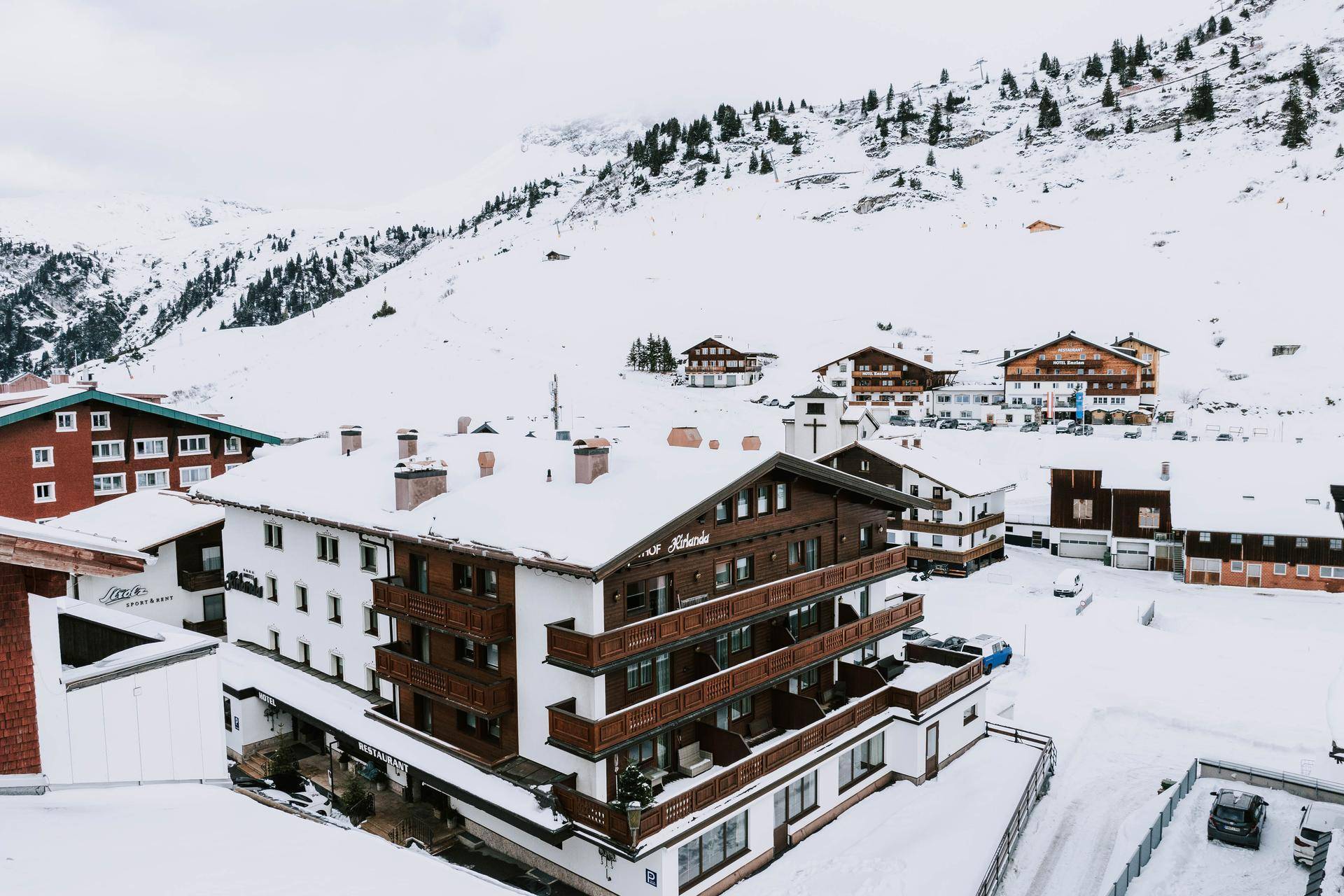 Panoramablick auf das verschneite Bergdorf mit dem Hotel Kirlana und umliegenden Gebäuden.