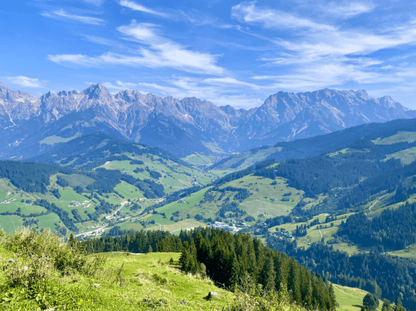 Weitläufige Berglandschaft mit grünen Tälern und bewaldeten Hängen unter blauem Himmel.