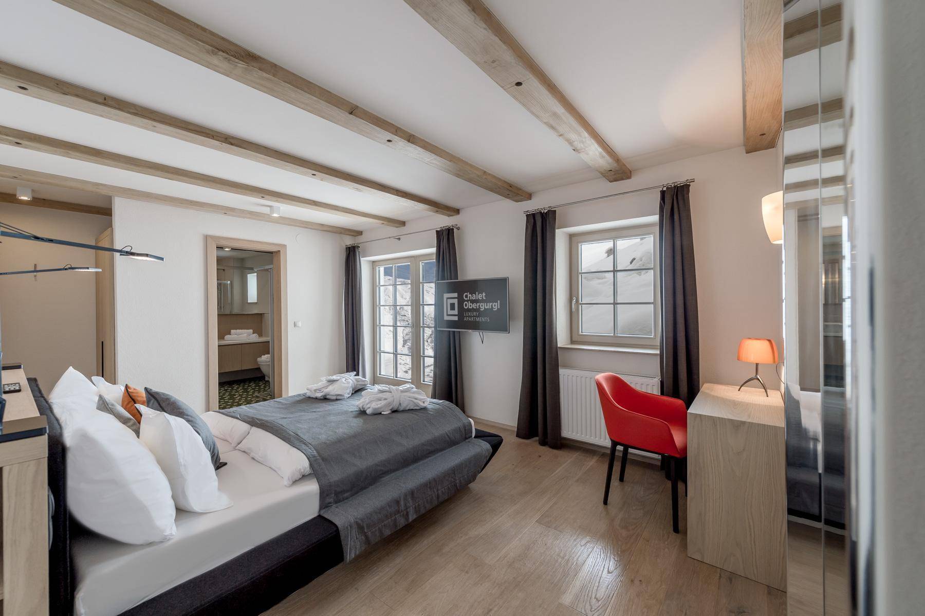 Gemütliches Schlafzimmer mit Holzbalken, Doppelbett und Zugang zu einem Balkon mit Bergblick.