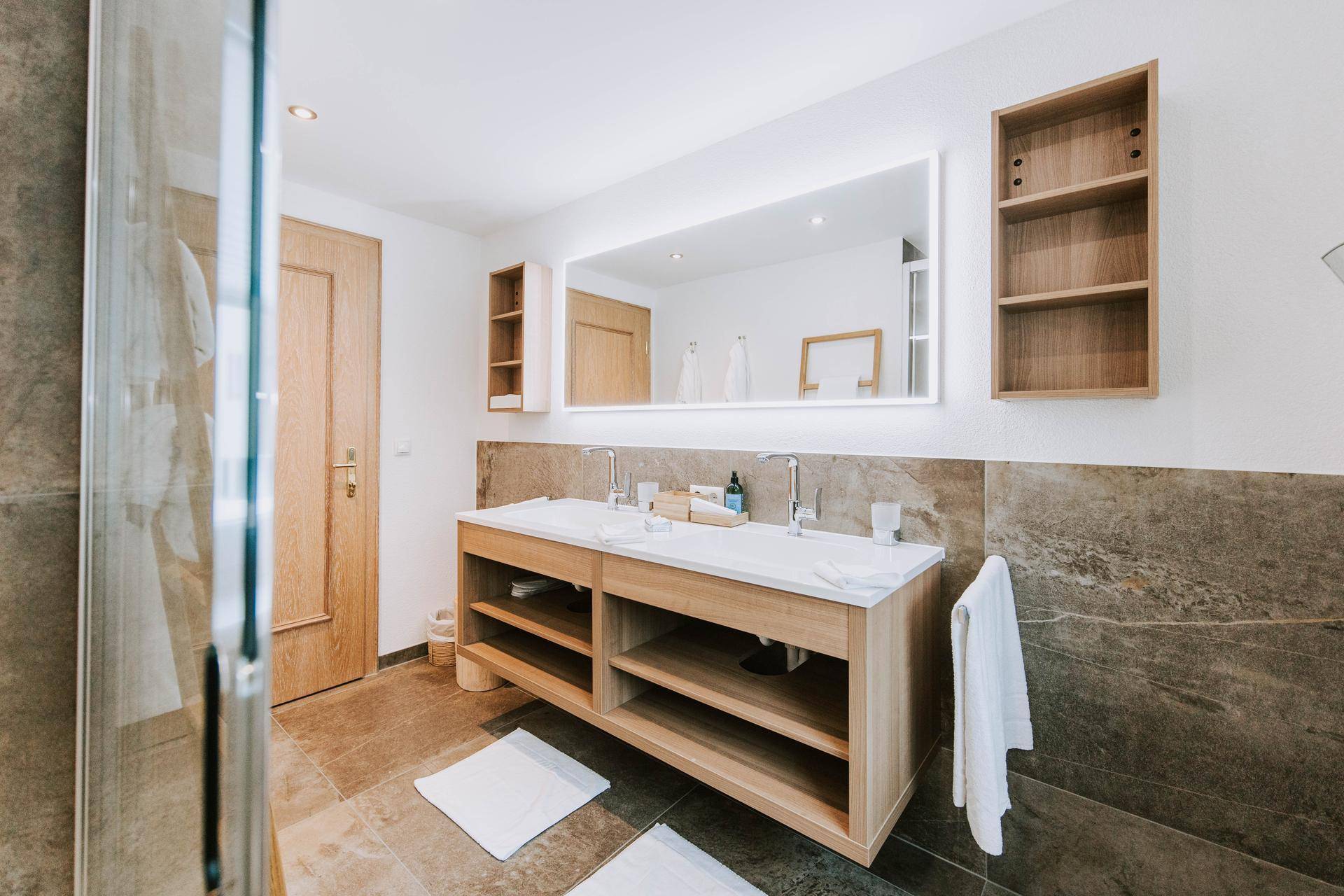 Geräumiges Badezimmer mit Doppelwaschtisch, großem beleuchteten Spiegel und begehbarer Dusche.