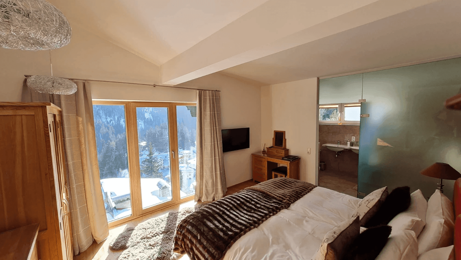 Lichtdurchflutetes Schlafzimmer mit Holzboden, Bergblick und offenem Zugang zum Badezimmer.