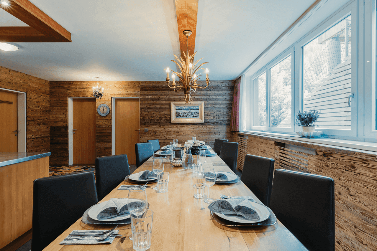 Heller Essbereich mit großer Holztafel, Holzwänden und Fenstern für viel Tageslicht.