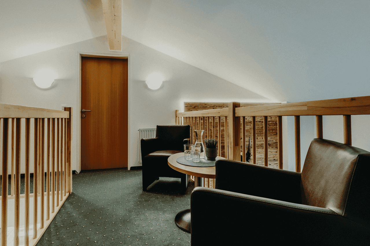 Gemütlicher Loftbereich mit Ledersesseln, Holztisch und schrägen Decken.