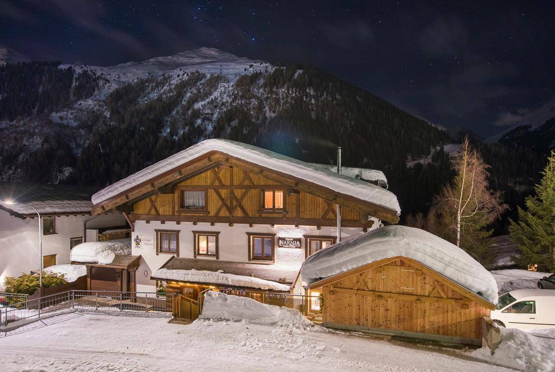 Traditionelles Chalet im alpinen Stil, umgeben von Schnee und Bergen unter klarem Nachthimmel.