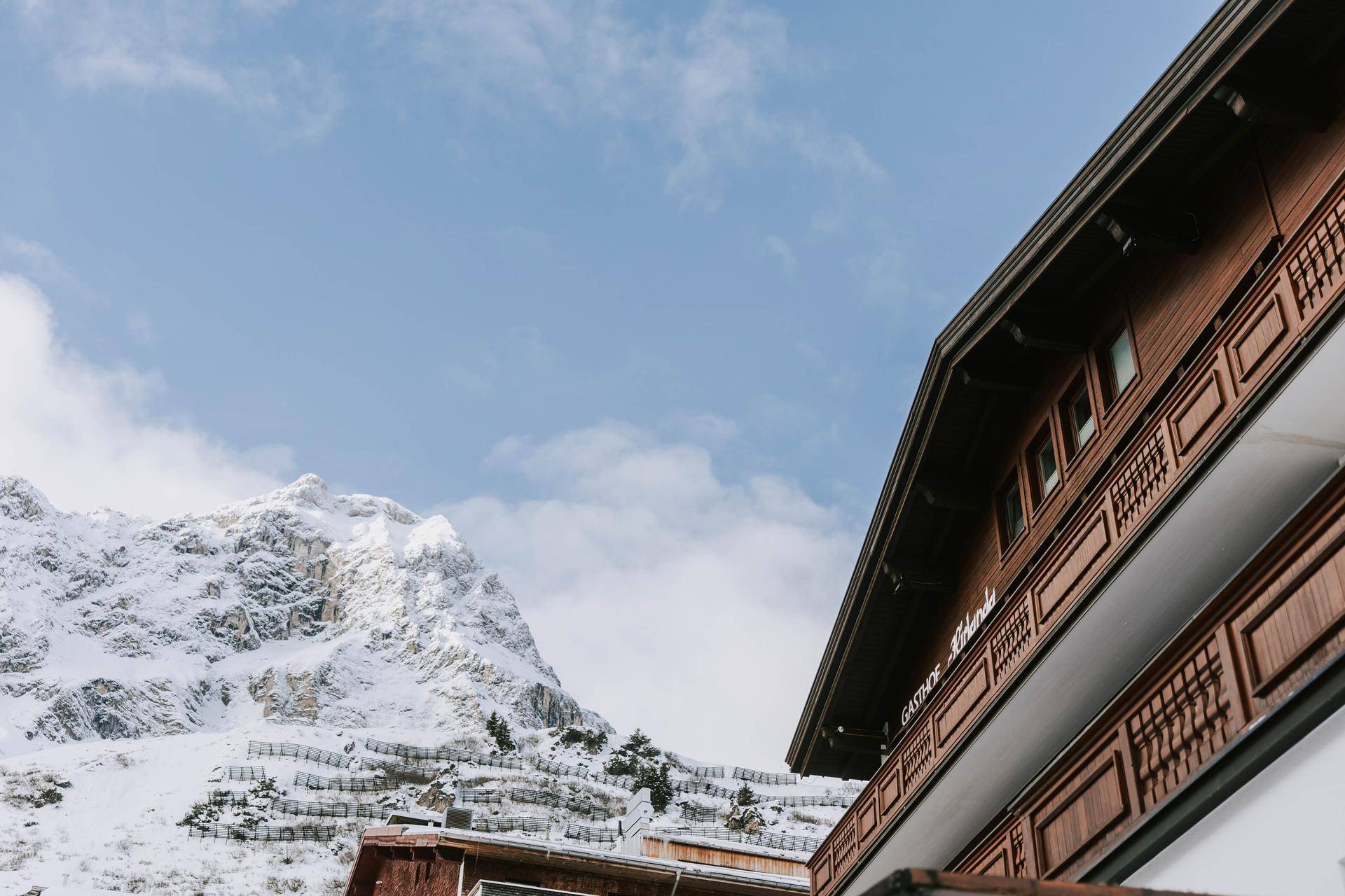 Traditionelle Holzfassade des Gasthofs Kirlana mit Blick auf die majestätischen schneebedeckten Berge.