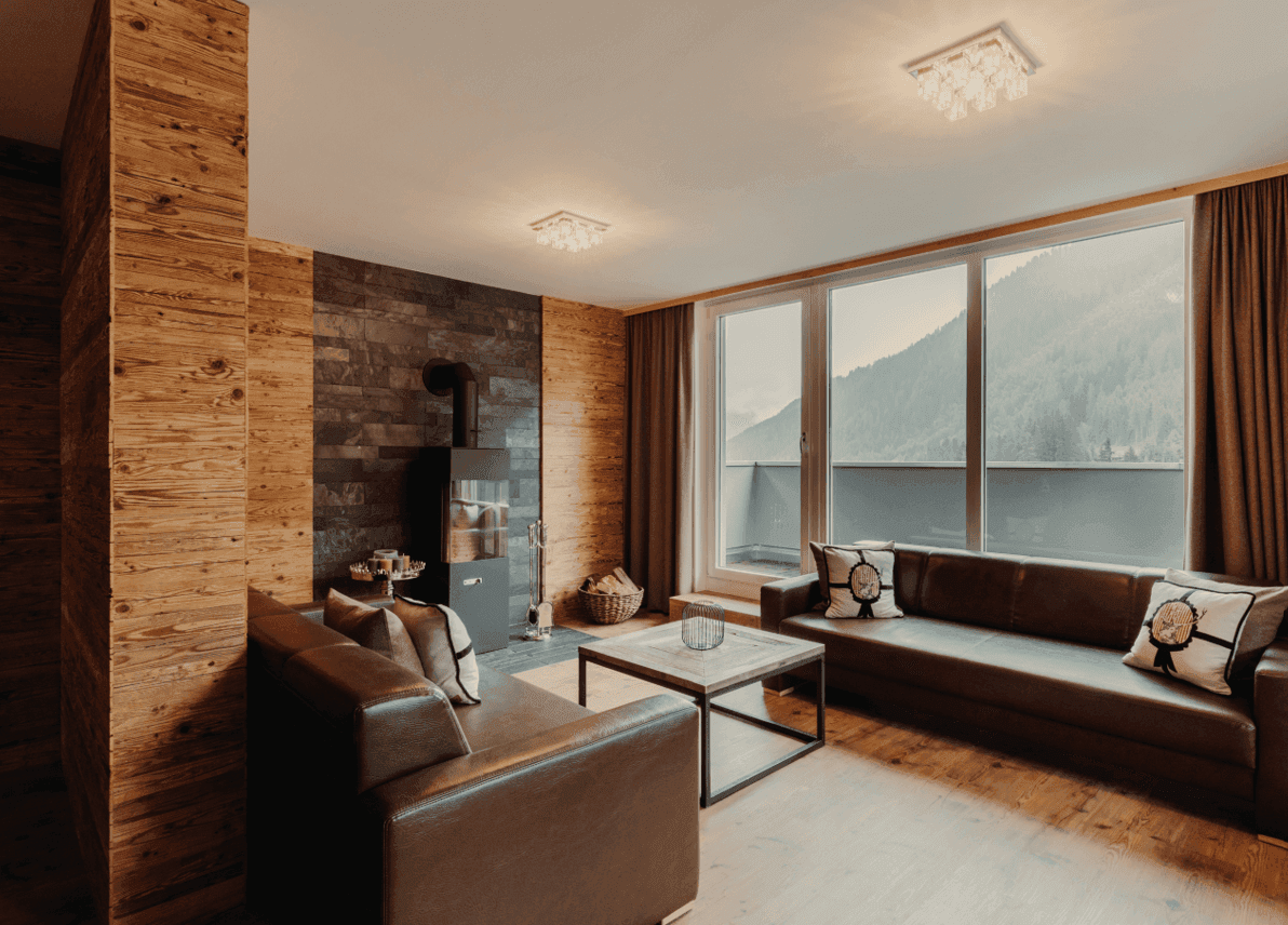 Gemütliches Wohnzimmer mit Holzwänden, modernem Kaminofen und großem Fenster mit Bergblick.