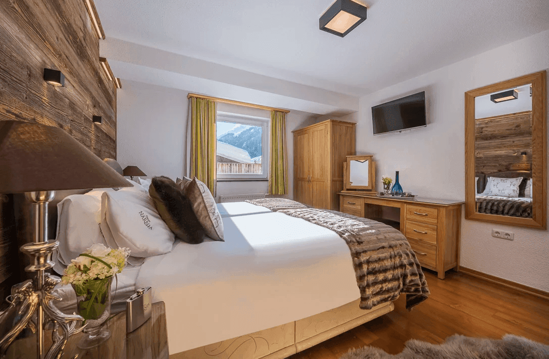 Helles Schlafzimmer mit Holzboden, großem Spiegel und Fensterblick auf die Berge.