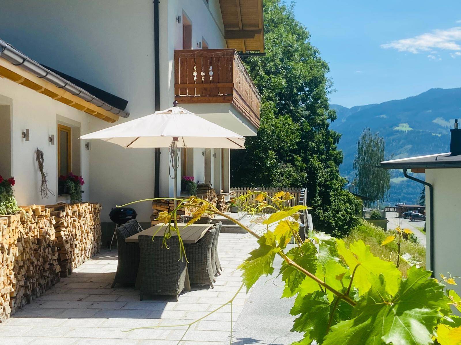 Sonniger Terrassenbereich mit Esstisch, Sonnenschirm und Blick auf die umliegende Berglandschaft.