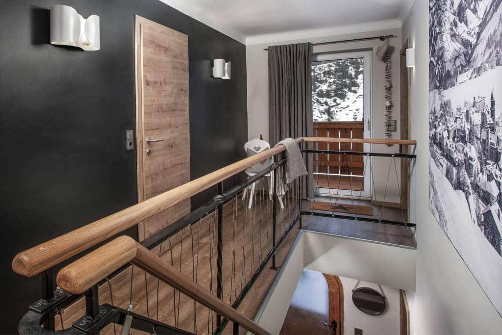 Heller Flur mit Holzgeländer, dunkler Akzentwand und Zugang zu einem kleinen Balkon.