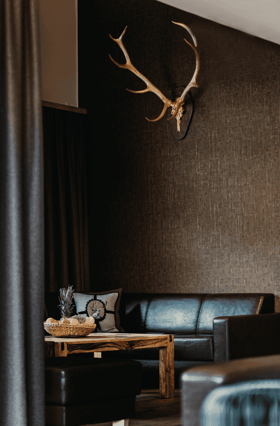 Dunklerer Wohnbereich mit Ledersofa, Holztisch und traditioneller Hirschgeweih-Dekoration.