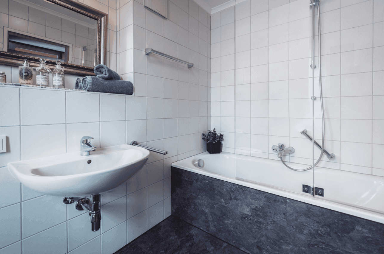 Detailansicht des Badezimmers mit Waschbecken, Badewanne und weißen Wandfliesen.