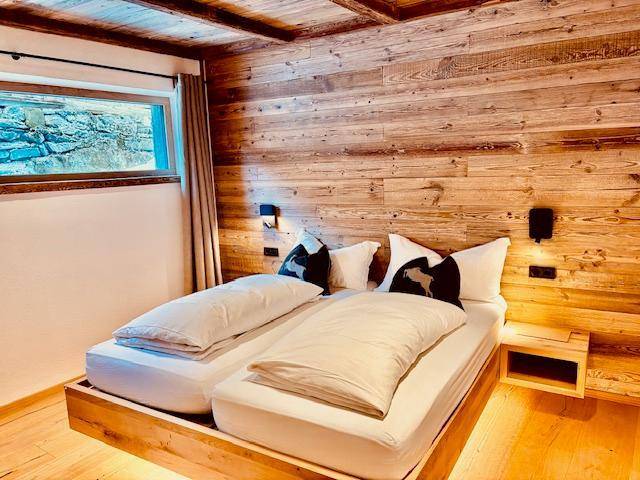 Gemütliches Schlafzimmer mit Holzwänden, Holzboden und einem kleinen Fenster, das viel Wärme ausstrahlt.