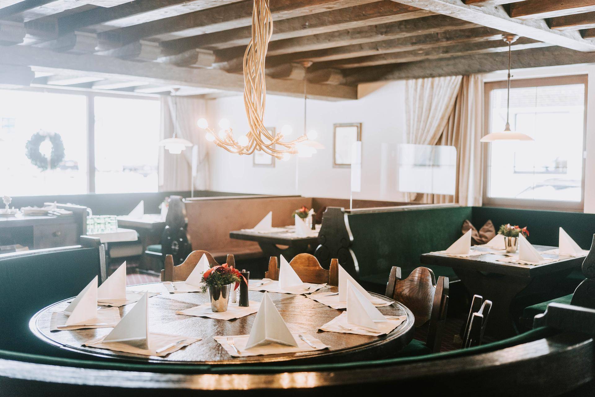 Traditioneller Restaurantbereich mit runden Tischen, gepolsterten Bänken und Holzbalkendecke.