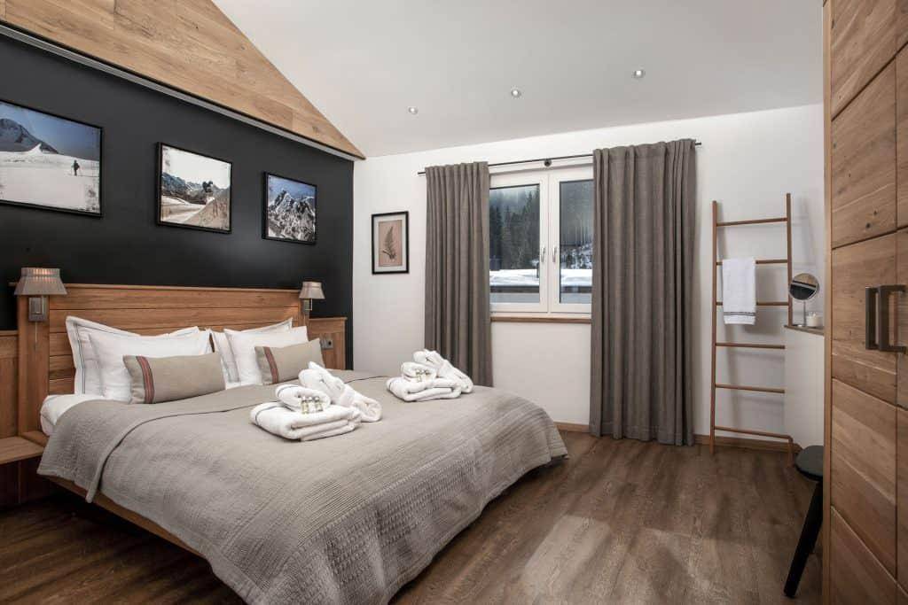 Geräumiges Schlafzimmer mit Holzbett, dunkler Akzentwand und Blick auf die verschneite Landschaft.