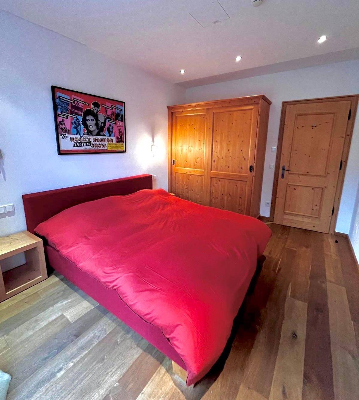 Schlafzimmer mit rotem Bett, Holzboden und großem Holzschrank in rustikalem Stil.